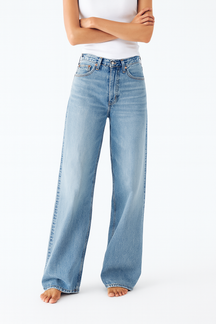 woman wearing blue jeans standing against light background