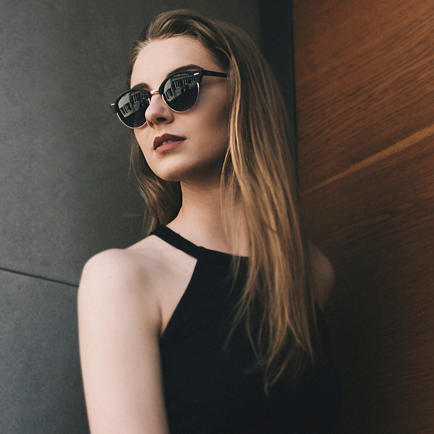 Girl standing against wall wearing black sunglasses